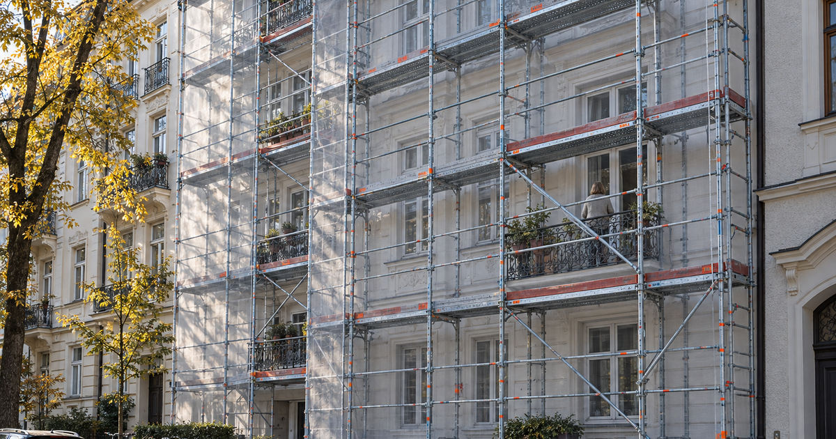 Eingerüstetes Gründerzeit-Mietshaus im Herbst, teils mit Schutznetz, eine Person auf dem Balkon von hinten